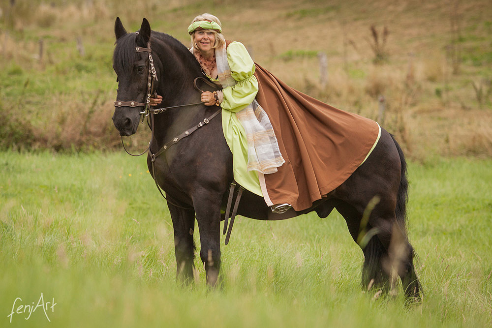 Pferdeshooting mit fenjArt Fotografie Blonde Reiterin sitzt in einem gruenen Kleid auf einem Friesenpferd